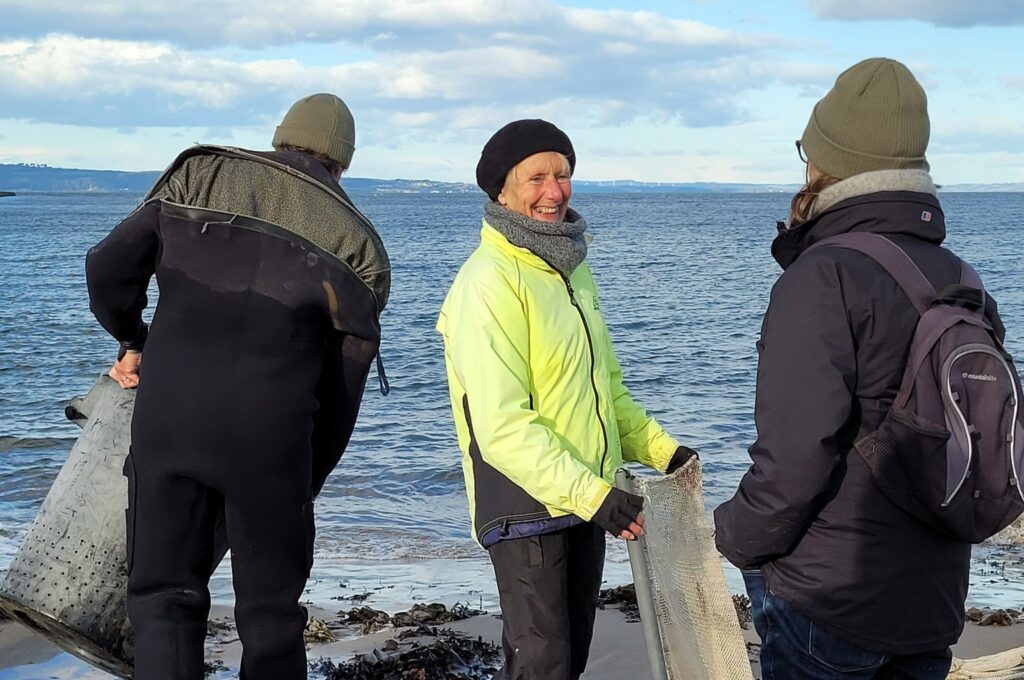 group of people collecting items on beach wearing wooly hats and jackets